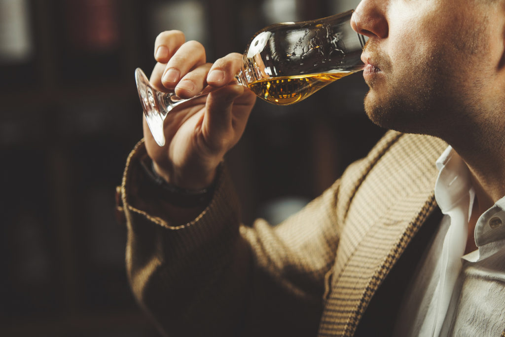 Close-up photo of sommelier tasting whiskey taste on the cellar background.