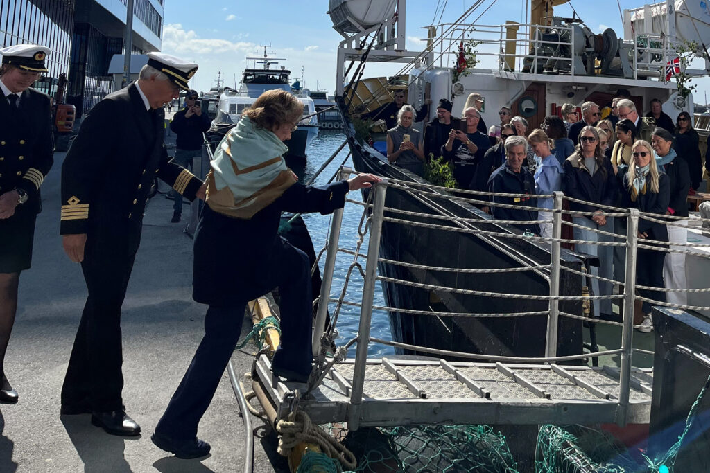 Bilde av dronning Sonja som går ombord i MS Salten, mens sjøfolk hjelper henne og publikum følger spent med